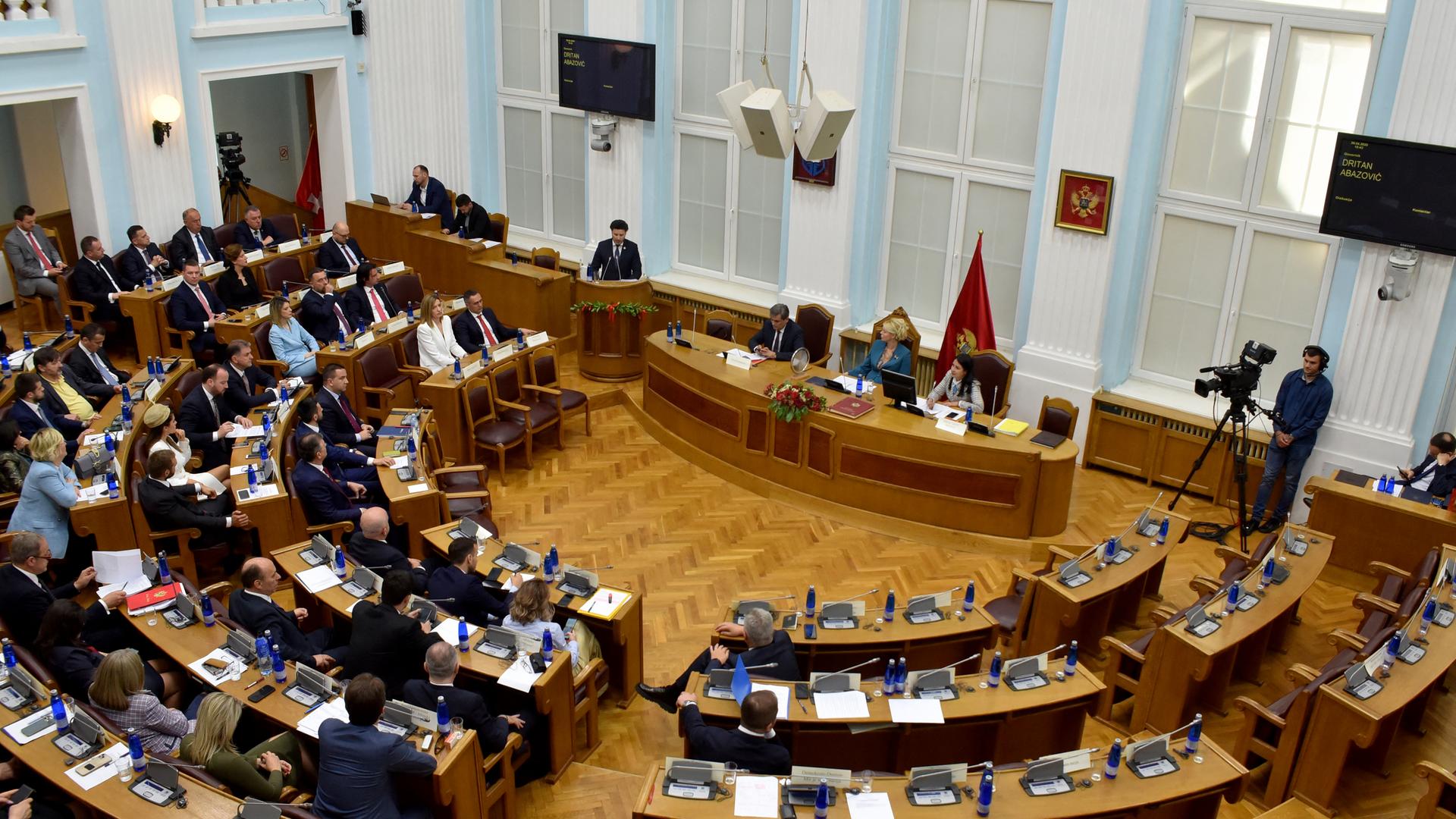 Der Blick auf das montenegrinische Parlament von oben. Holzvertäfelte Sitzreihen sind im Halbkreis auf das Rednerpult ausgerichtet. Der Blick auf das montenegrinische Parlament von oben. Holzvertäfelte Sitzreihen sind im Halbkreis auf das Rednerpult ausgerichtet.