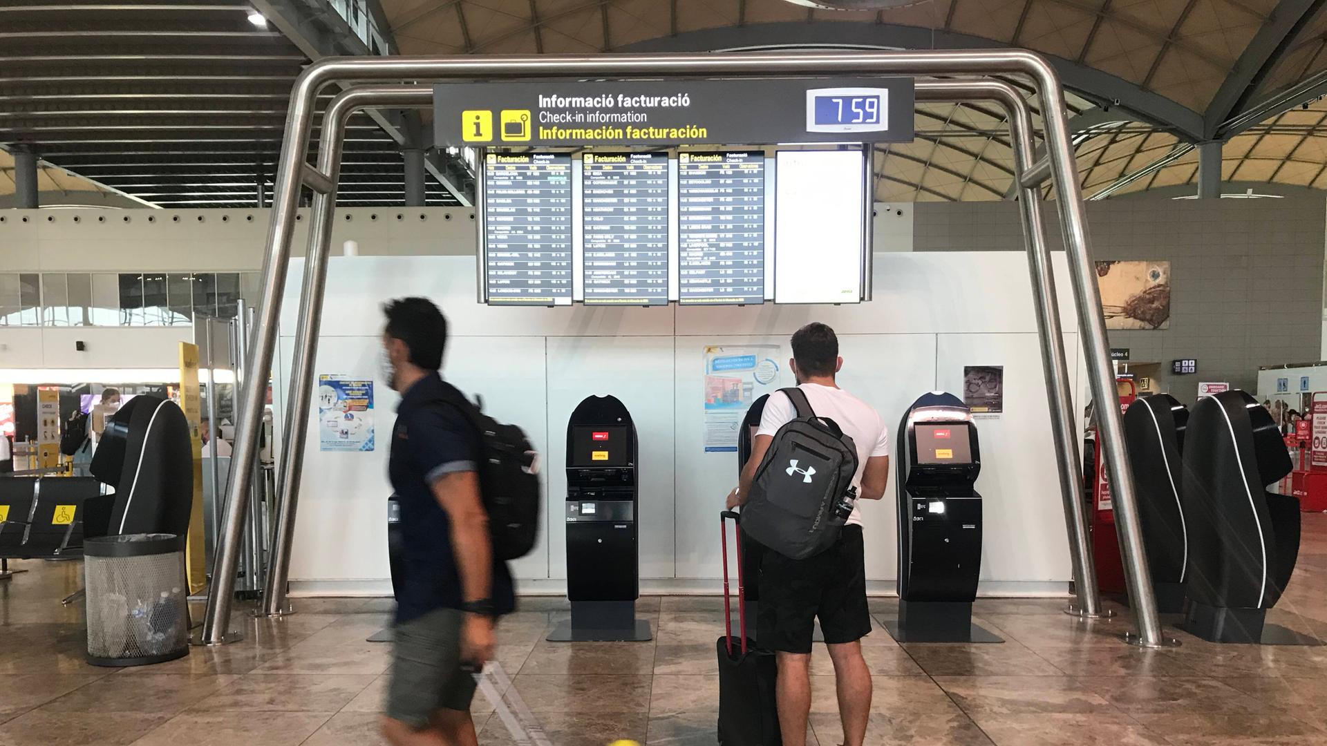 Fluggäste stehen im Terminal des Flughafens Alicante vor Bildschirmen Fluggäste stehen im Terminal des Flughafens Alicante vor Bildschirmen