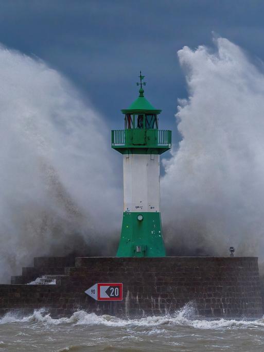 Hohe Wellen schlagen gegen einen grün-weißen Leuchtturm auf der Ostmole an der Ostseeküste, wo sich im Oktober 2023 eine schwere Sturmflut ereignete.