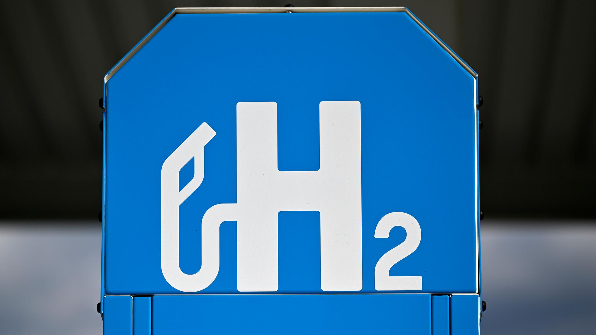 Ein blaues Schild mit dem Symbol "H2" an der Zapfsäule einer Wasserstofftankstelle 