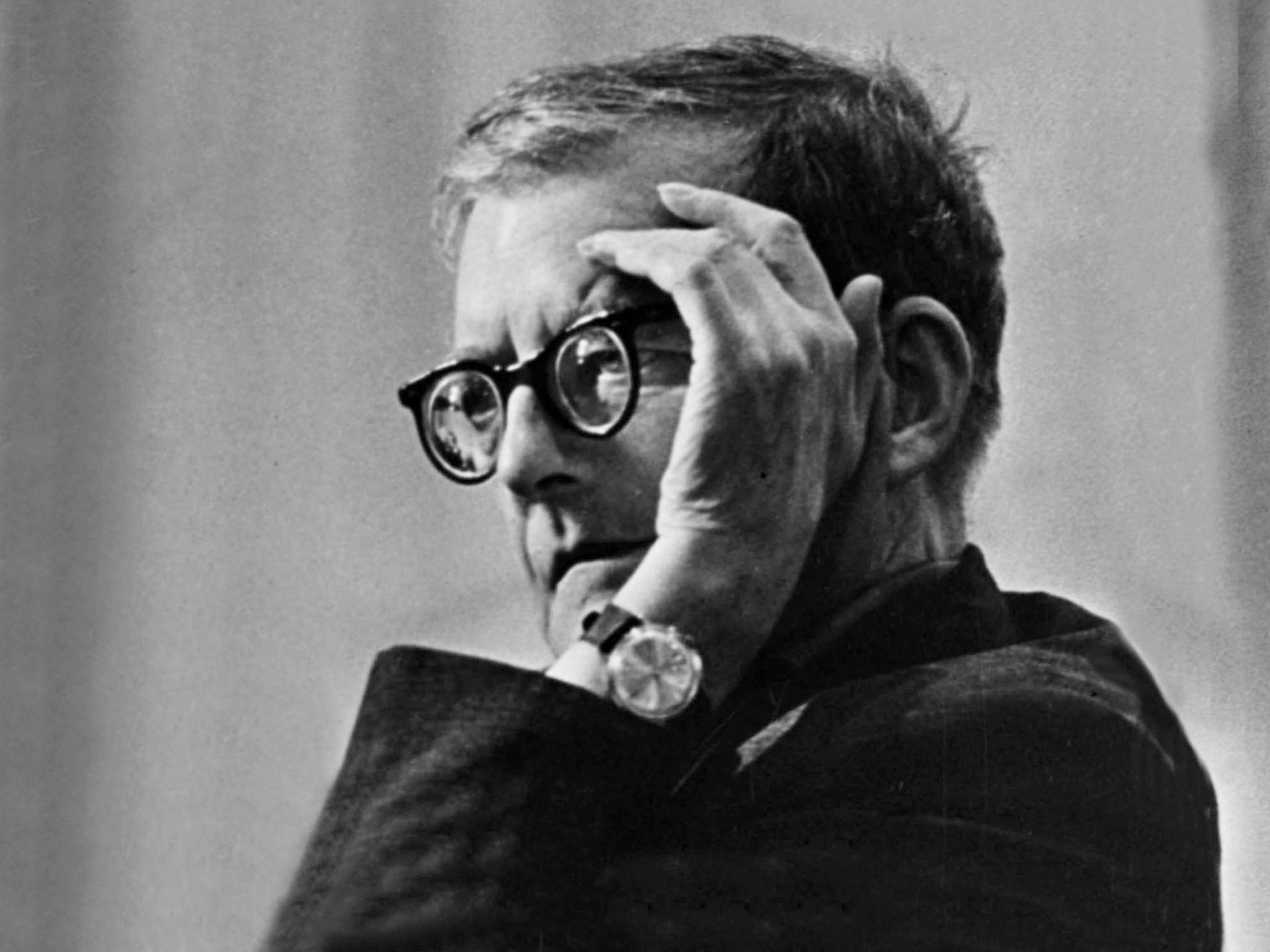 Dmitri Shostakovich sitzt mit aufgestütztem Ellebogen so, dass eine Hand sein Gesicht ein wenig abschirmt. 