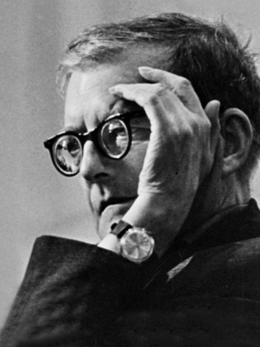Dmitri Shostakovich sitzt mit aufgestütztem Ellebogen so, dass eine Hand sein Gesicht ein wenig abschirmt. 
