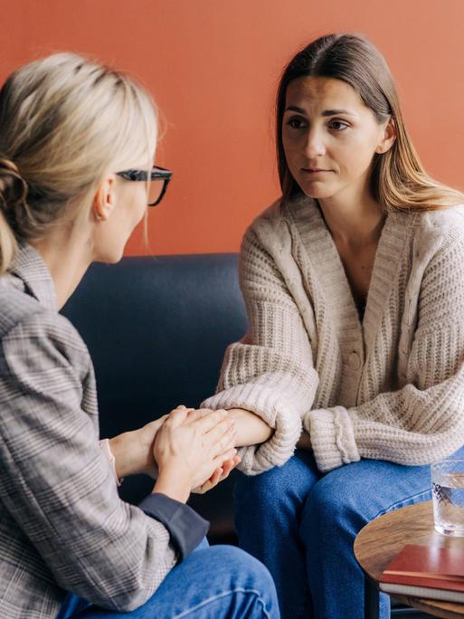 Zwei Frauen sitzen auf einem Sofa und unterhalten sich vertraulich.