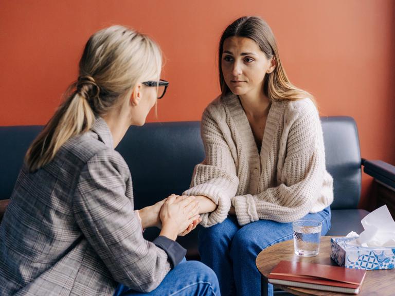 Zwei Frauen sitzen auf einem Sofa und unterhalten sich vertraulich.