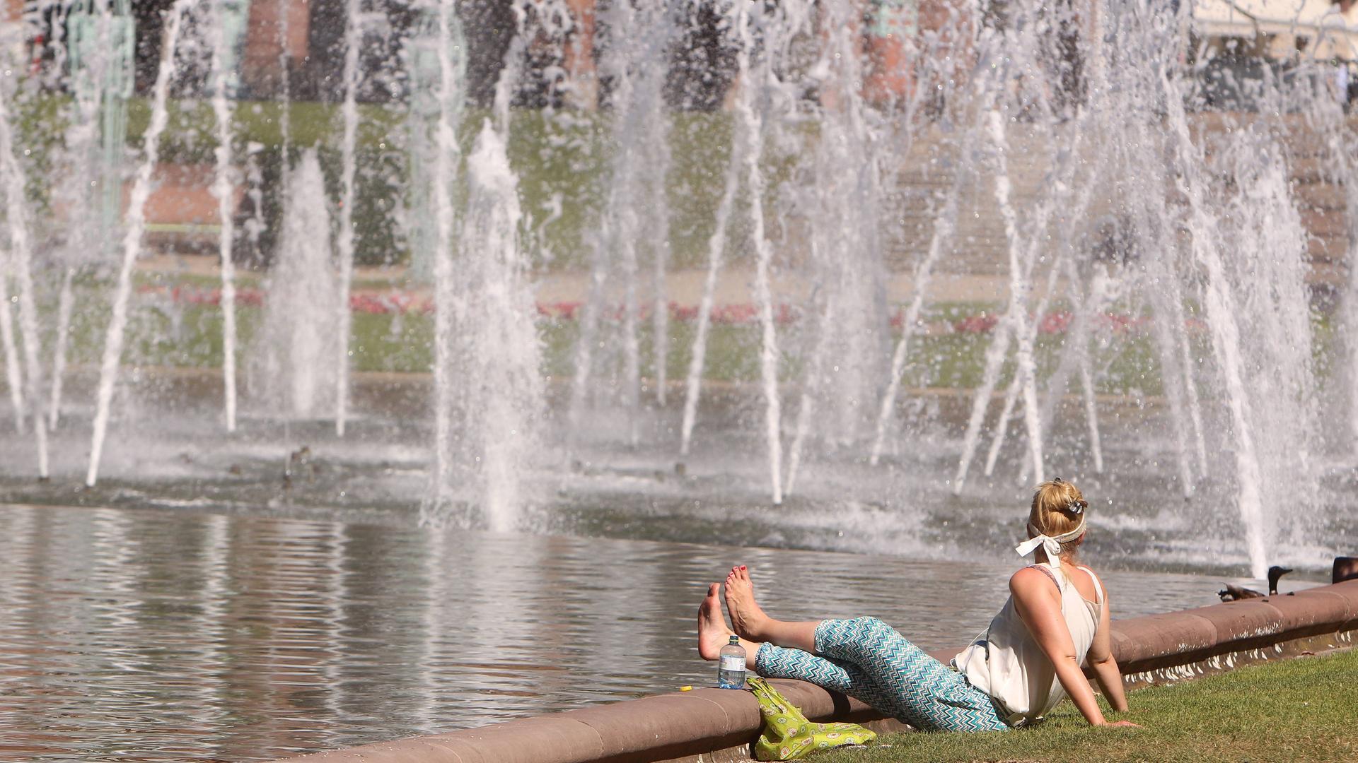 Frau sitzt an einem Springbrunnen im Rosengarten Mannheim. Symbolbild: Hitze in der Stadt Frau sitzt an einem Springbrunnen im Rosengarten Mannheim. Symbolbild: Hitze in der Stadt