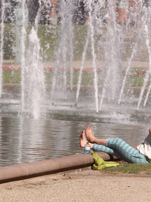 Frau sitzt an einem Springbrunnen im Rosengarten Mannheim. Symbolbild: Hitze in der Stadt