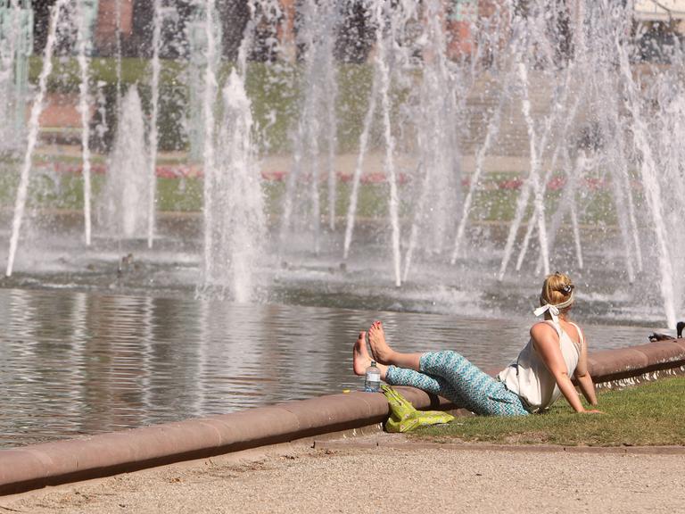 Frau sitzt an einem Springbrunnen im Rosengarten Mannheim. Symbolbild: Hitze in der Stadt