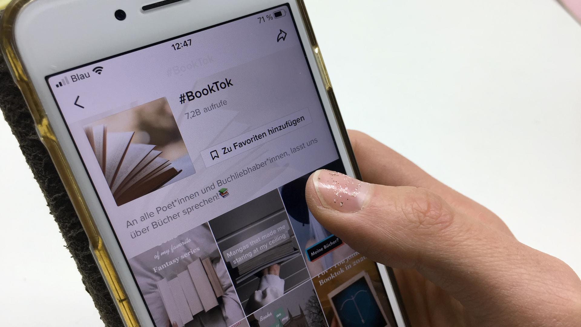 Eine Hand hält ein Smartphone, auf dem die Plattform #BookTook mit Buchempfehlungen bei TikTok geöffnet ist.