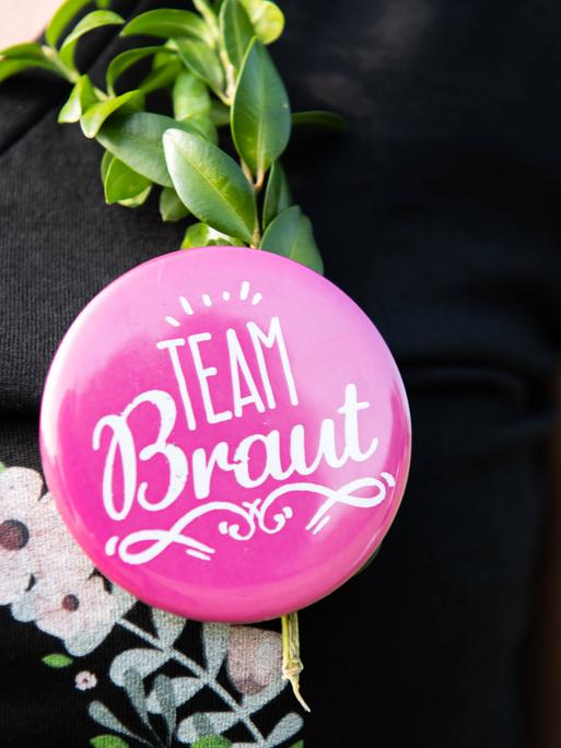 Eine Frau trägt bei einem Junggesellenabschied einen Button mit der Aufschrift Team Braut.