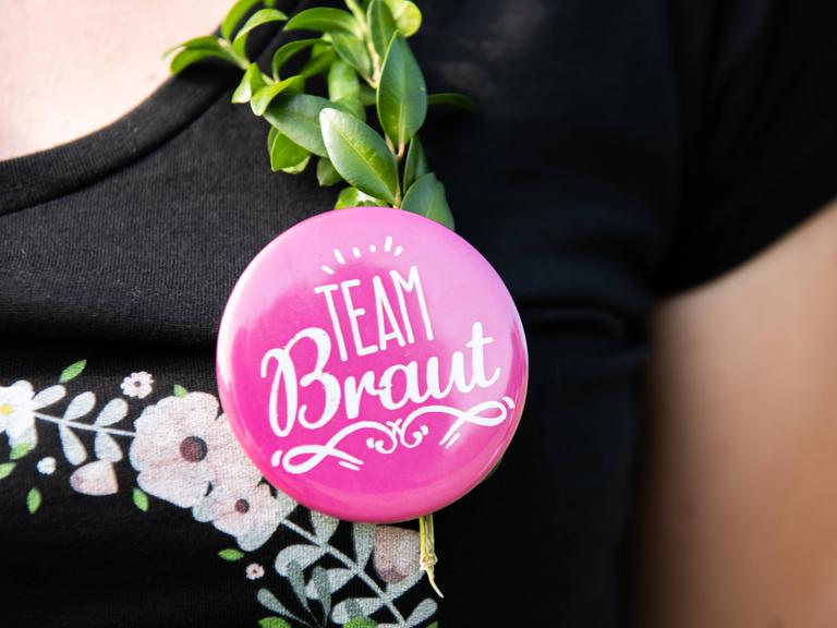Eine Frau trägt bei einem Junggesellenabschied einen Button mit der Aufschrift Team Braut.