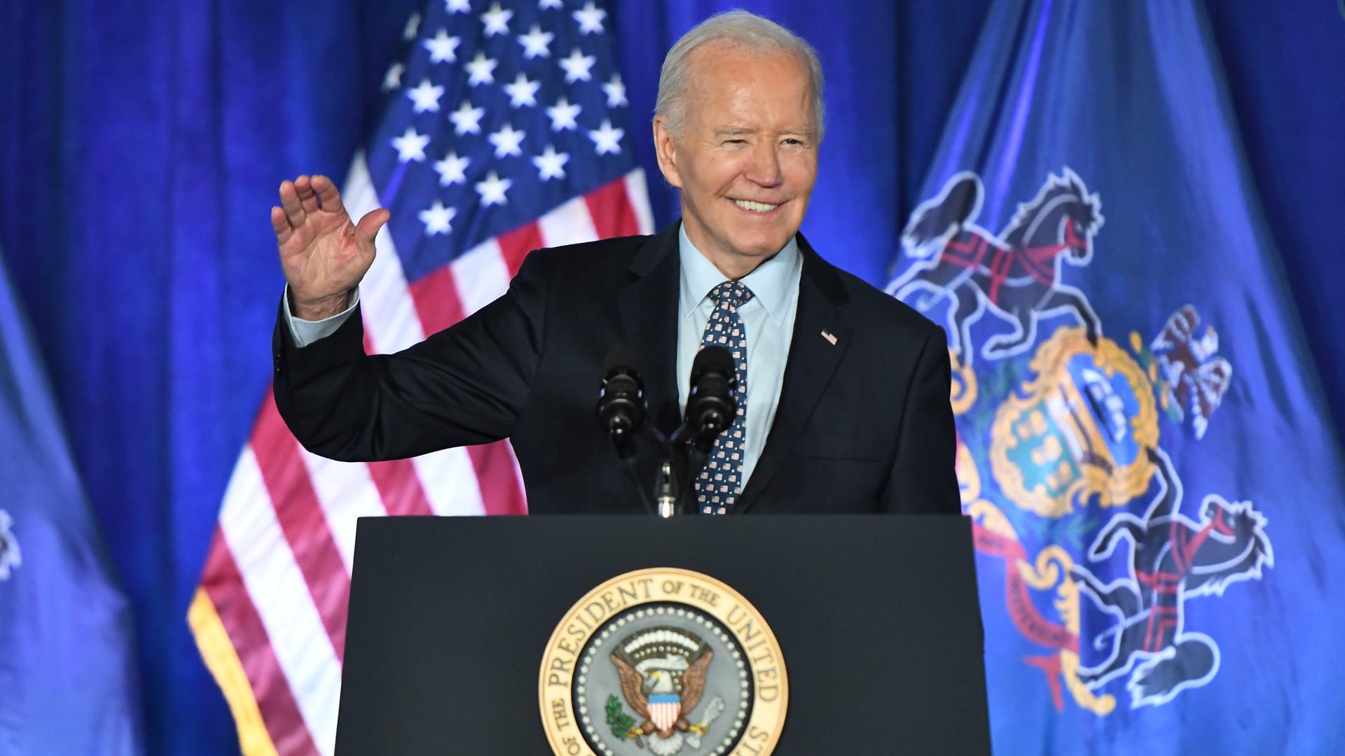 US-Präsident Joe Biden steht während einer Wahlkampfveranstaltung in Philadelphia an einem Redepult und erhebt die rechte Hand zum Gruß. 