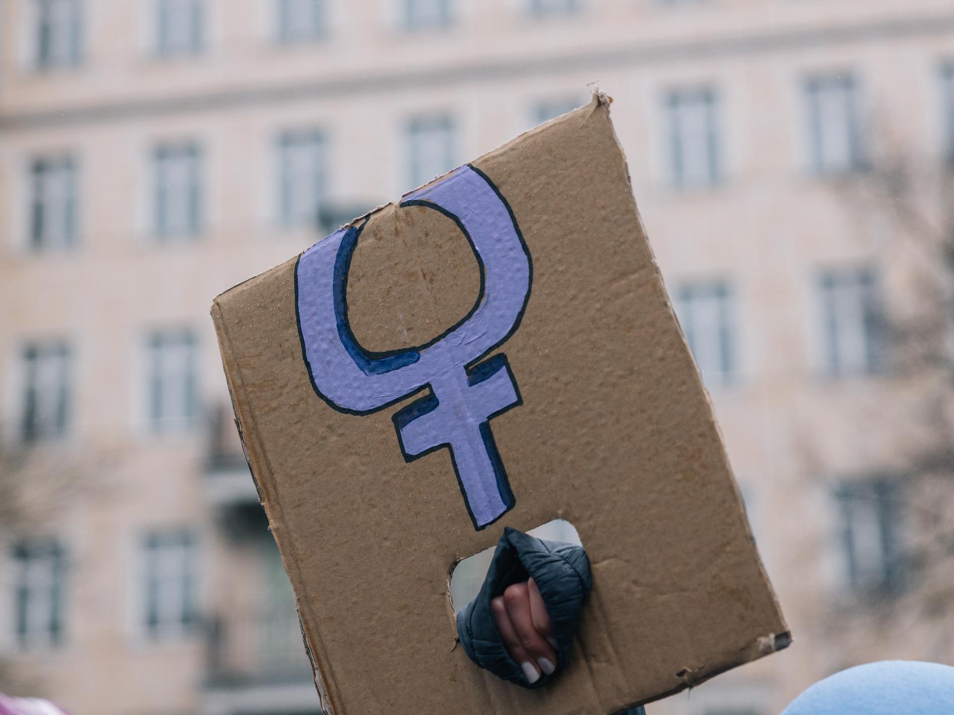 Eine Hand, die ein abgeknicktes Transparent mit dem violetten Symbol für Frauen hält