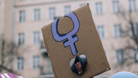 Eine Hand, die ein abgeknicktes Transparent mit dem violetten Symbol für Frauen hält