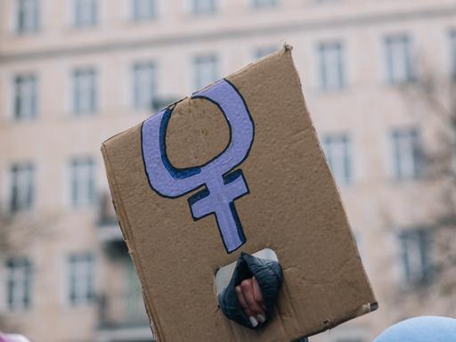 Eine Hand, die ein abgeknicktes Transparent mit dem violetten Symbol für Frauen hält