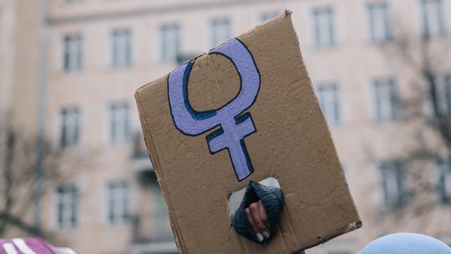 Eine Hand, die ein abgeknicktes Transparent mit dem violetten Symbol für Frauen hält