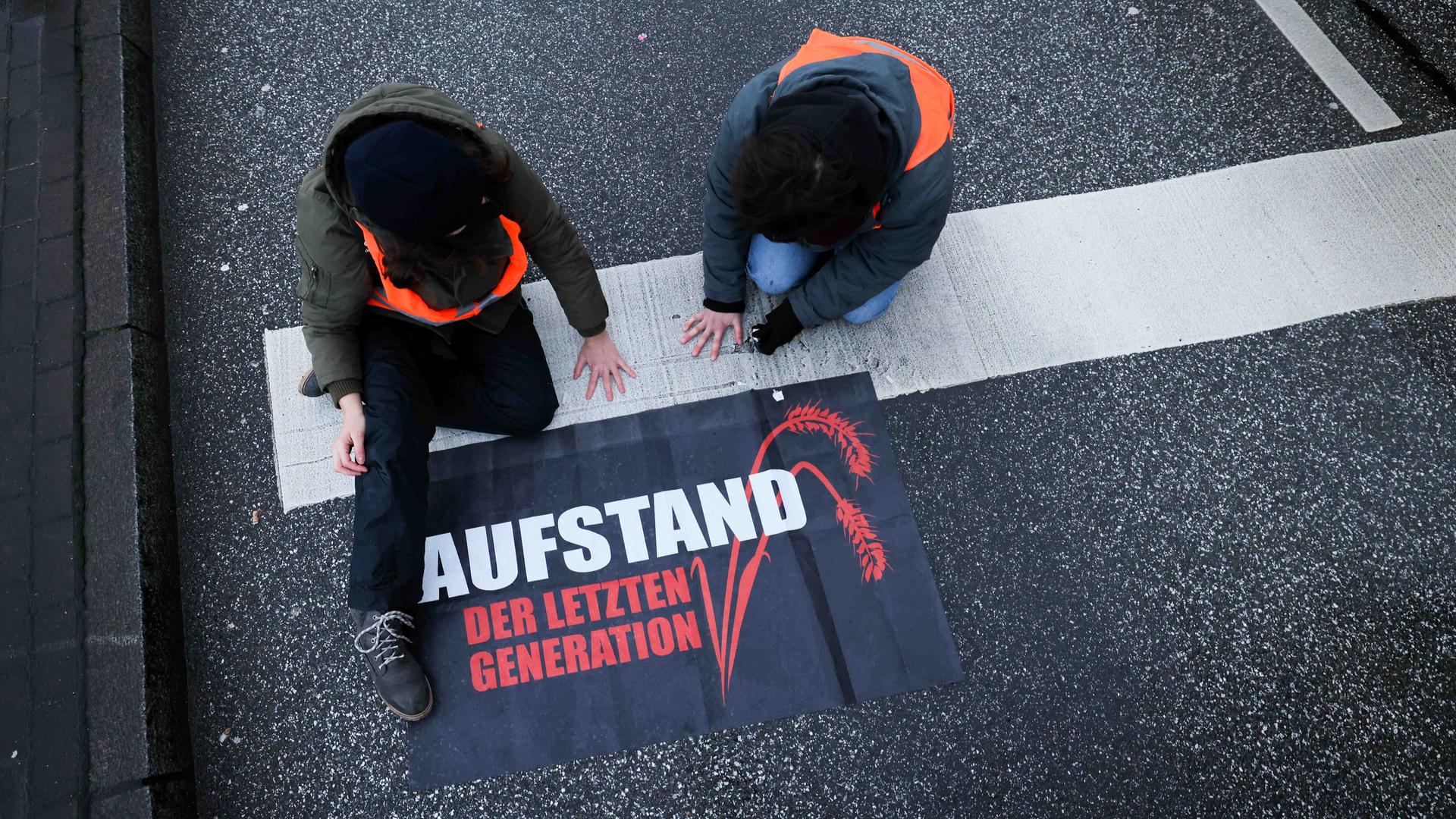 Klimaaktivisten der Gruppe "Aufstand der letzten Generation" haben ihre Hände in Hamburg auf die Straße geklebt. Neben ihnen liegt ein Transparent mit der Aufschrift: "Aufstand der letzten Generation".