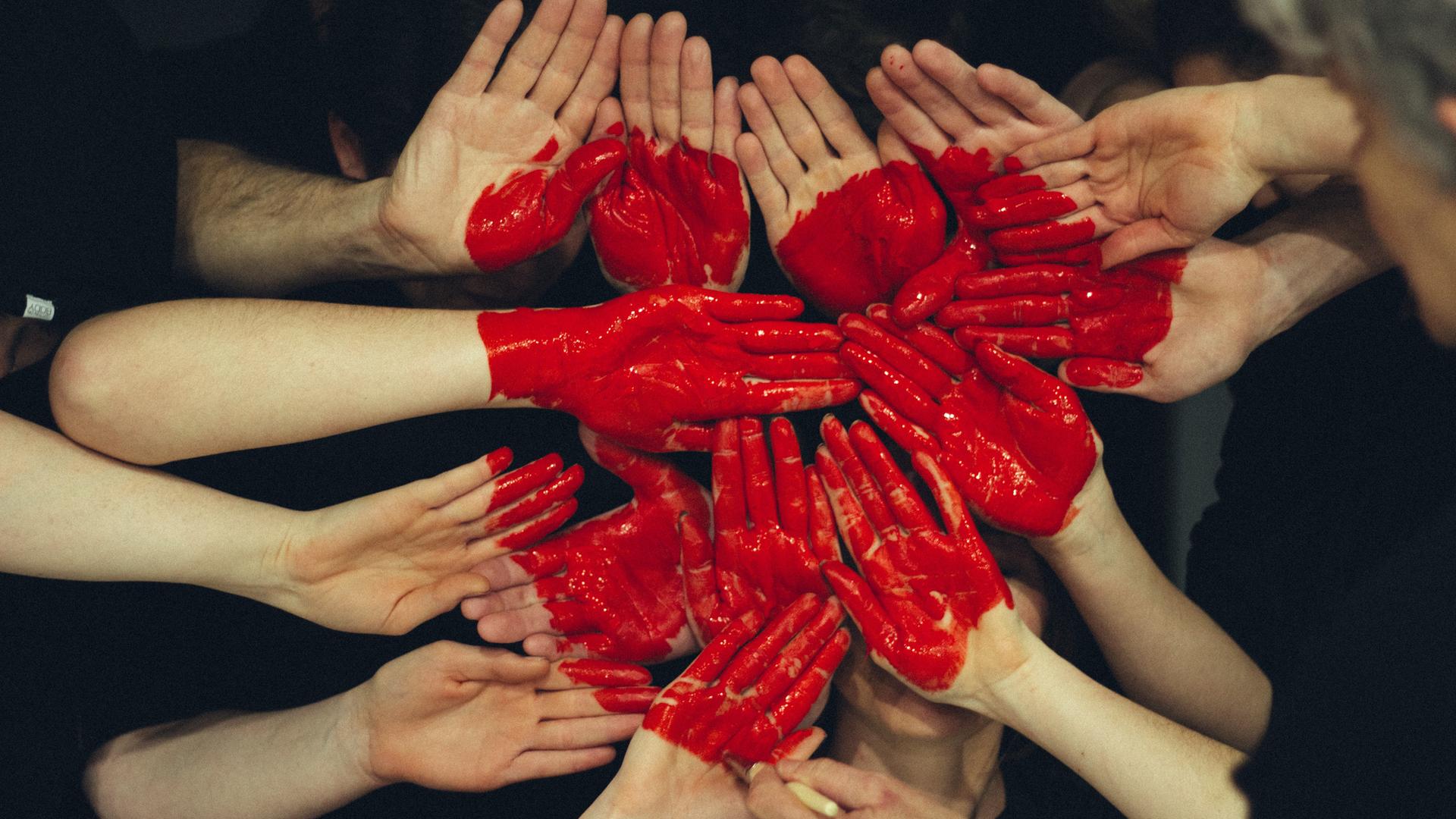Auf mehrere Hände gemalte rote Farbe stellt ein Herz dar. (Symbolfoto)
