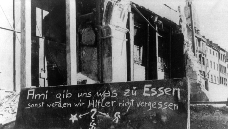 Auf einem Plakat vor den Trümmern Münchens steht:"Ami gibt uns was zu Essen sonst werden wir Hitler nicht vergessen", aufgenommen im Winter 1946/47.