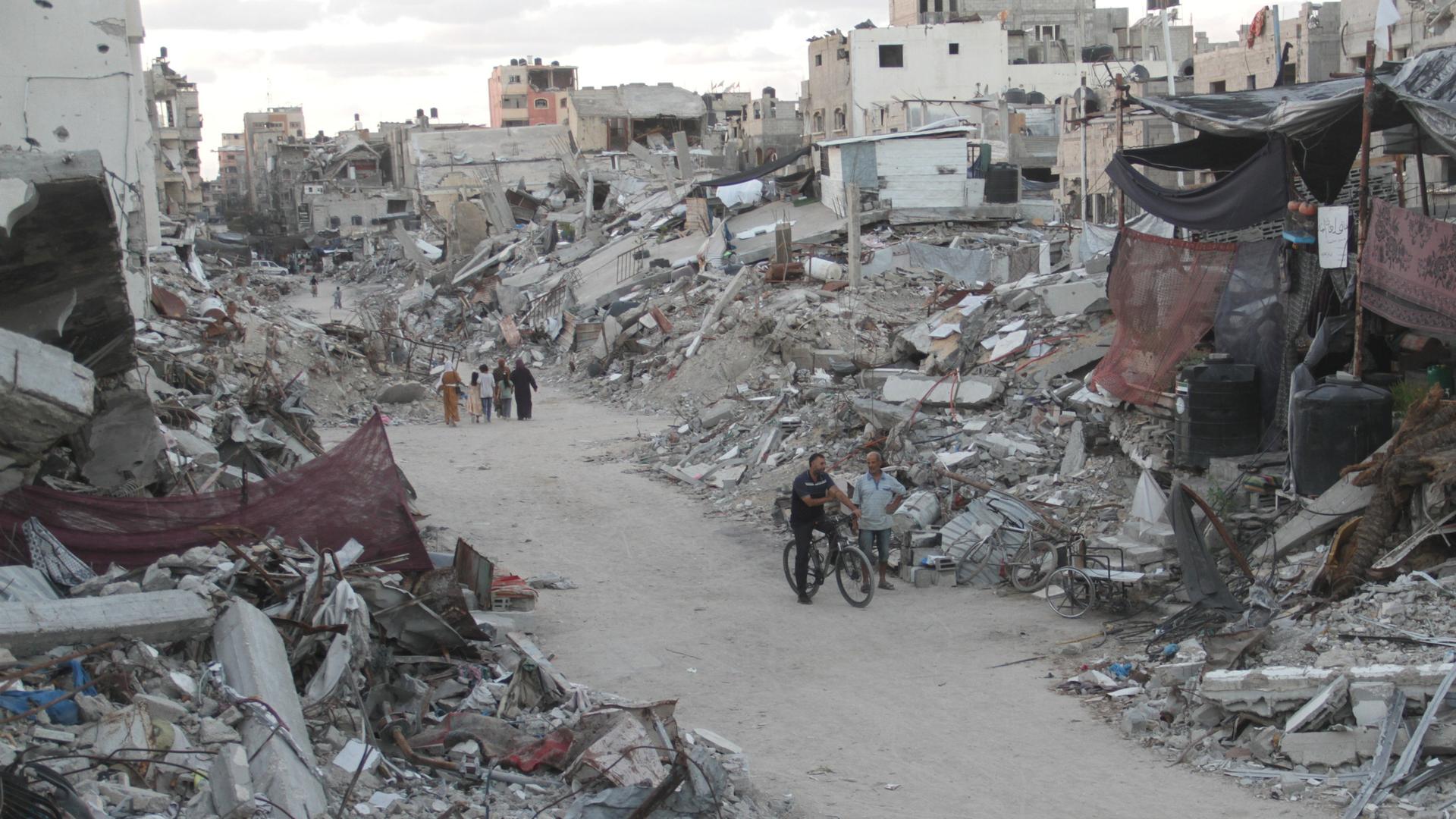 Menschen laufen auf einem Weg durch zerstörte Häuser im Gazastreifen.