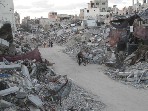 Menschen laufen auf einem Weg durch zerstörte Häuser im Gazastreifen.