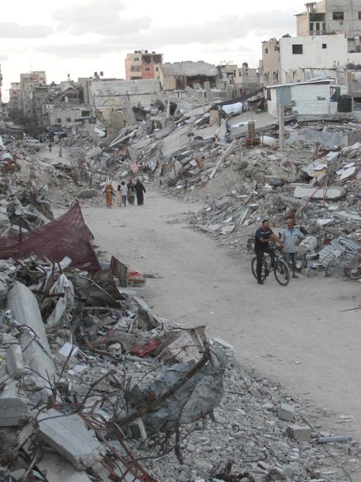 Menschen laufen auf einem Weg durch zerstörte Häuser im Gazastreifen.