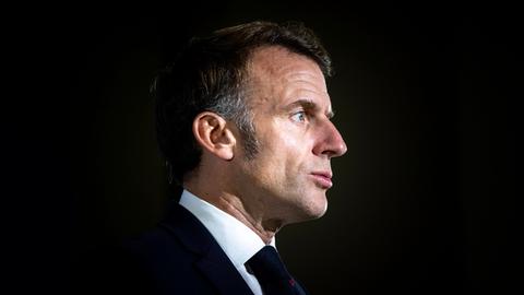 Präsident Emmanuel Macron im Anzug vor dunklem Hintergrund