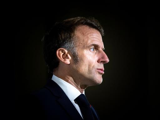 Präsident Emmanuel Macron im Anzug vor dunklem Hintergrund
