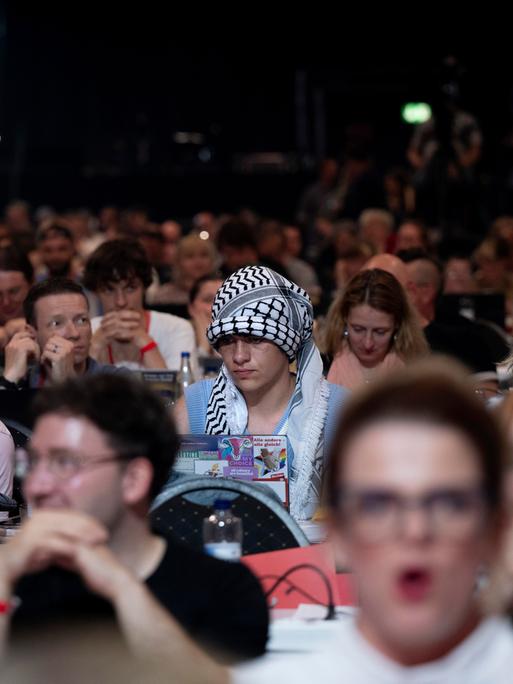 Ein Delegierter auf dem Parteitag der Linken sitzt unter Parteigenossen und hat ein Palästinensertuch als Symbol der Solidarität mit Palästina um seinen Kopf gebunden.