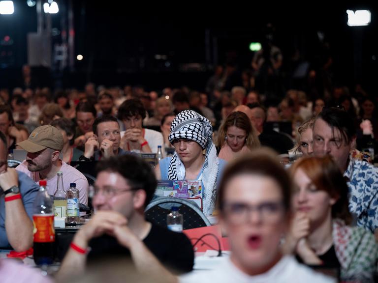 Ein Delegierter auf dem Parteitag der Linken sitzt unter Parteigenossen und hat ein Palästinensertuch als Symbol der Solidarität mit Palästina um seinen Kopf gebunden.