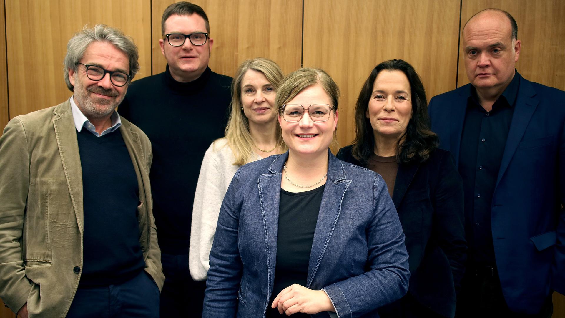 Die Podcaster Stephan Detjen, Ulf Buermeyer, Anne Will, Tina Hildebrandt, Nadine Lindner und Robin Alexander (v.l.n.r.) stehen vor einer Studiowand.