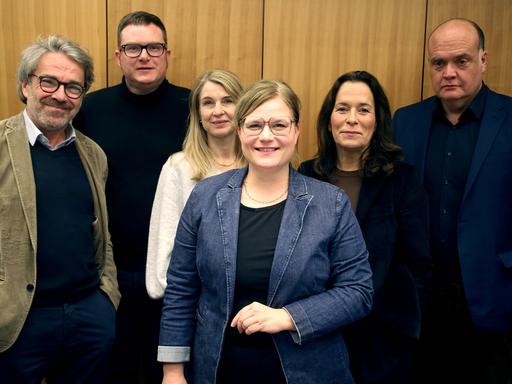 Die Podcaster Stephan Detjen, Ulf Buermeyer, Anne Will, Tina Hildebrandt, Nadine Lindner und Robin Alexander (v.l.n.r.) stehen vor einer Studiowand.