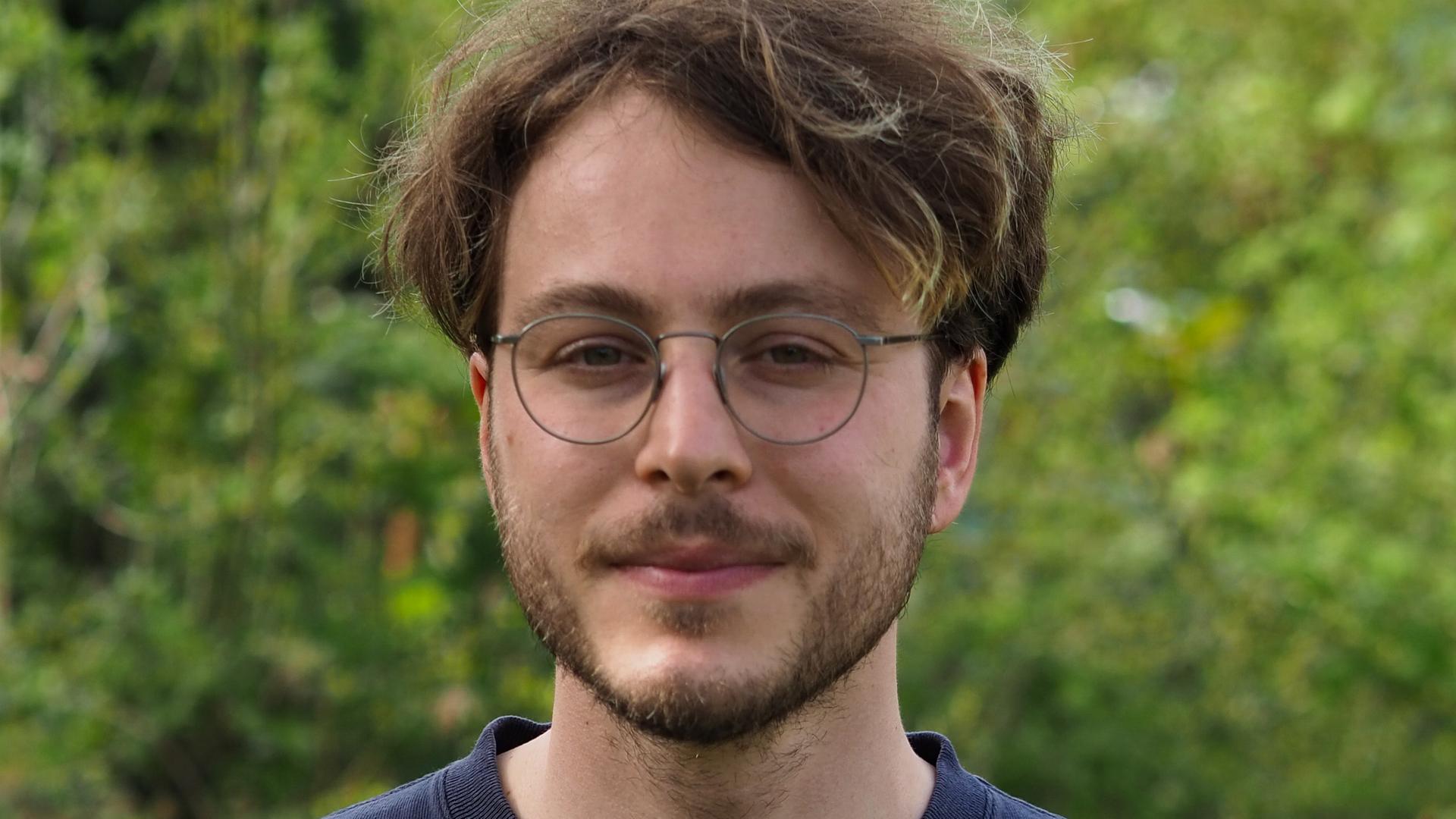 Marco Ott trägt eine Brille und Bart, steht in einem grünen Garten und schaut freundlich in die Kamera.