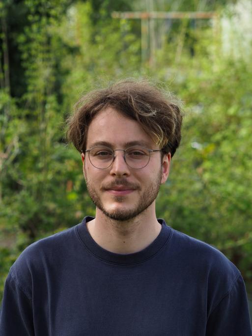 Marco Ott trägt eine Brille und Bart, steht in einem grünen Garten und schaut freundlich in die Kamera.