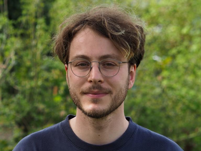 Marco Ott trägt eine Brille und Bart, steht in einem grünen Garten und schaut freundlich in die Kamera.