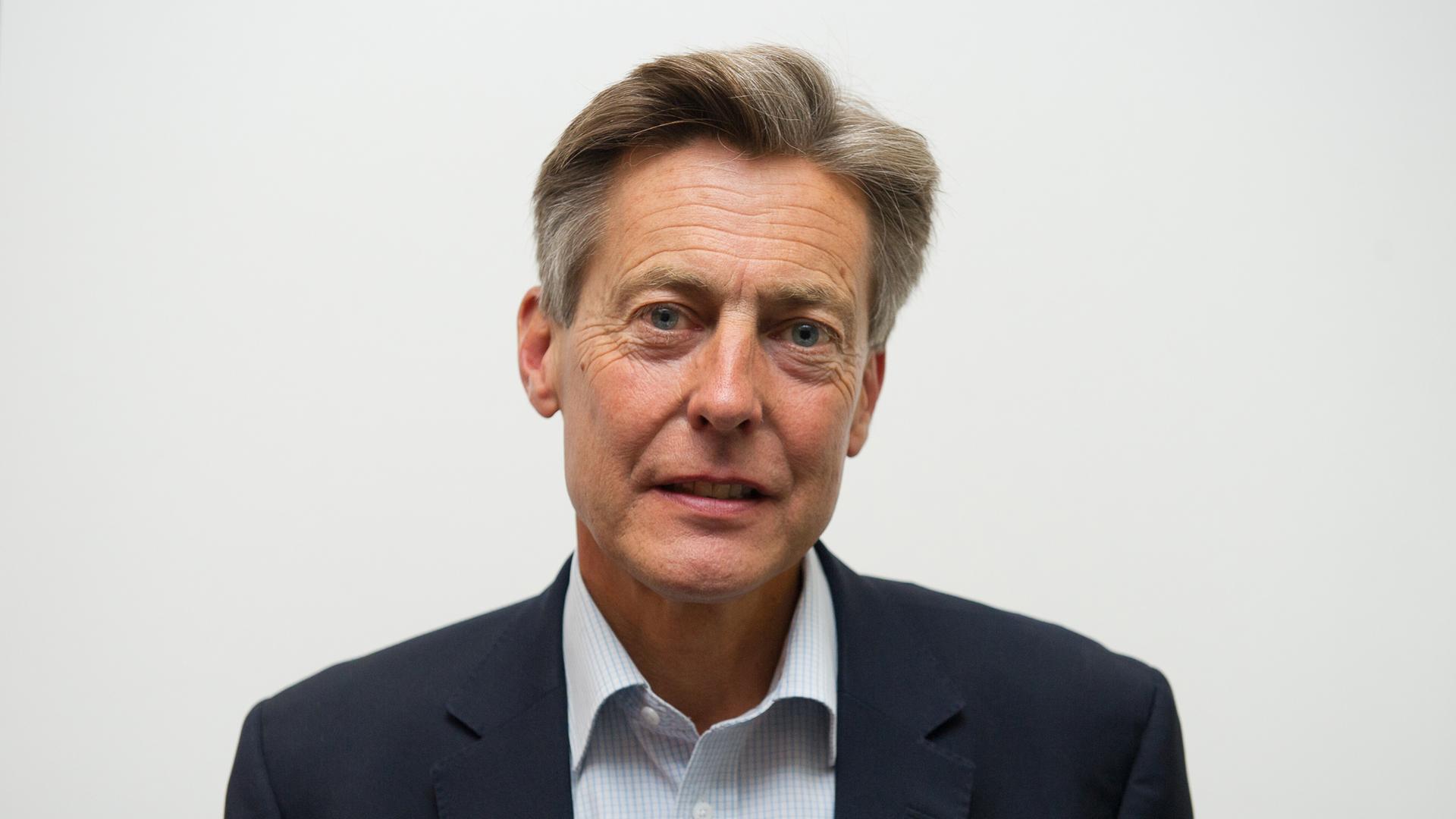 Ben Bradshaw steht vor einem weißen Hintergrund. Er trägt ein Hemd und ein Jackett.