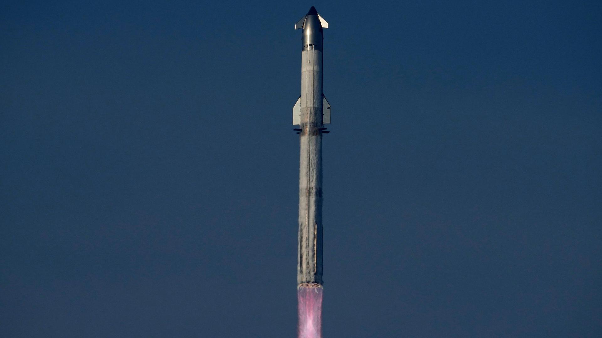 Das Bild zeigt eine startende Starship-Rakete, an deren unteren Ende der glühende Feuerschweif des Brennstoff-Antriebs zu sehen ist. Das Bild zeigt eine startende Starship-Rakete, an deren unteren Ende der glühende Feuerschweif des Brennstoff-Antriebs zu sehen ist.