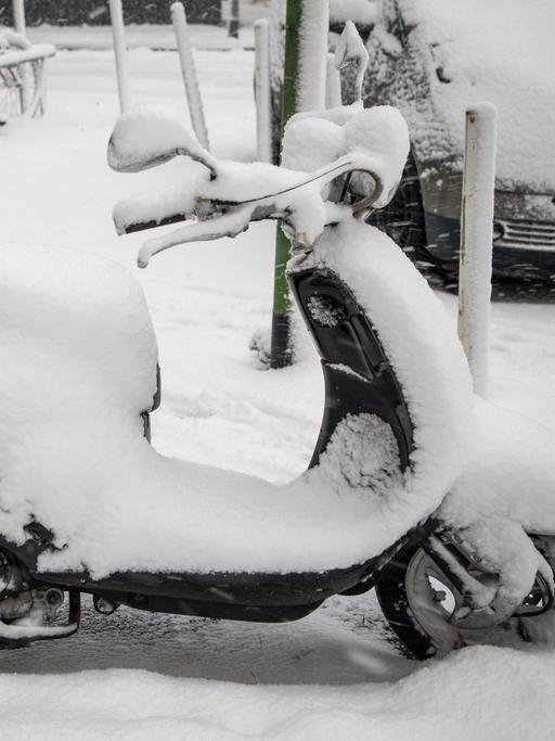 Ein verschneiter Motorroller steht am Straßenrand.