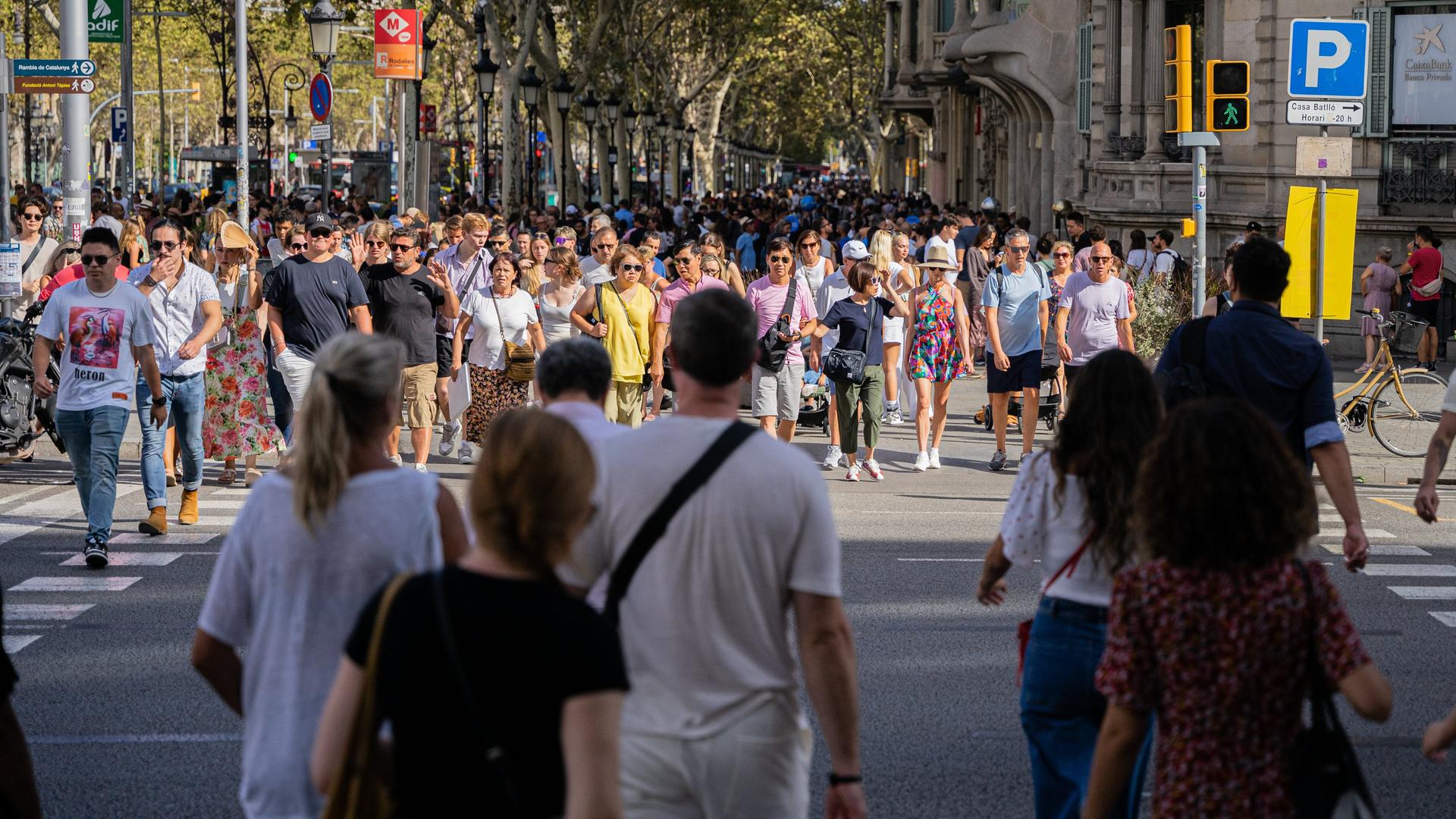 Hunderte Touristen laufen über eine Straße in der Stadt Barcelona. 