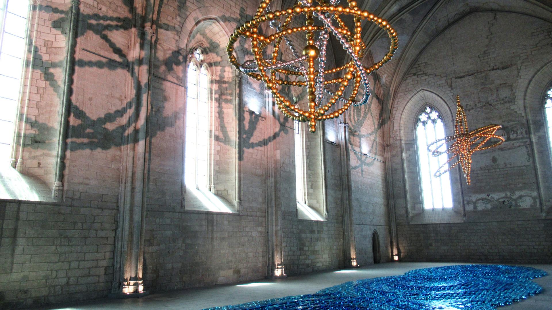 Ein Werk des Künstlers Jean-Michel Othoniel mit blauem Glas am Boden und goldenen Perlen als Leuchter in einem Raum des Papstpalastes in Avignon