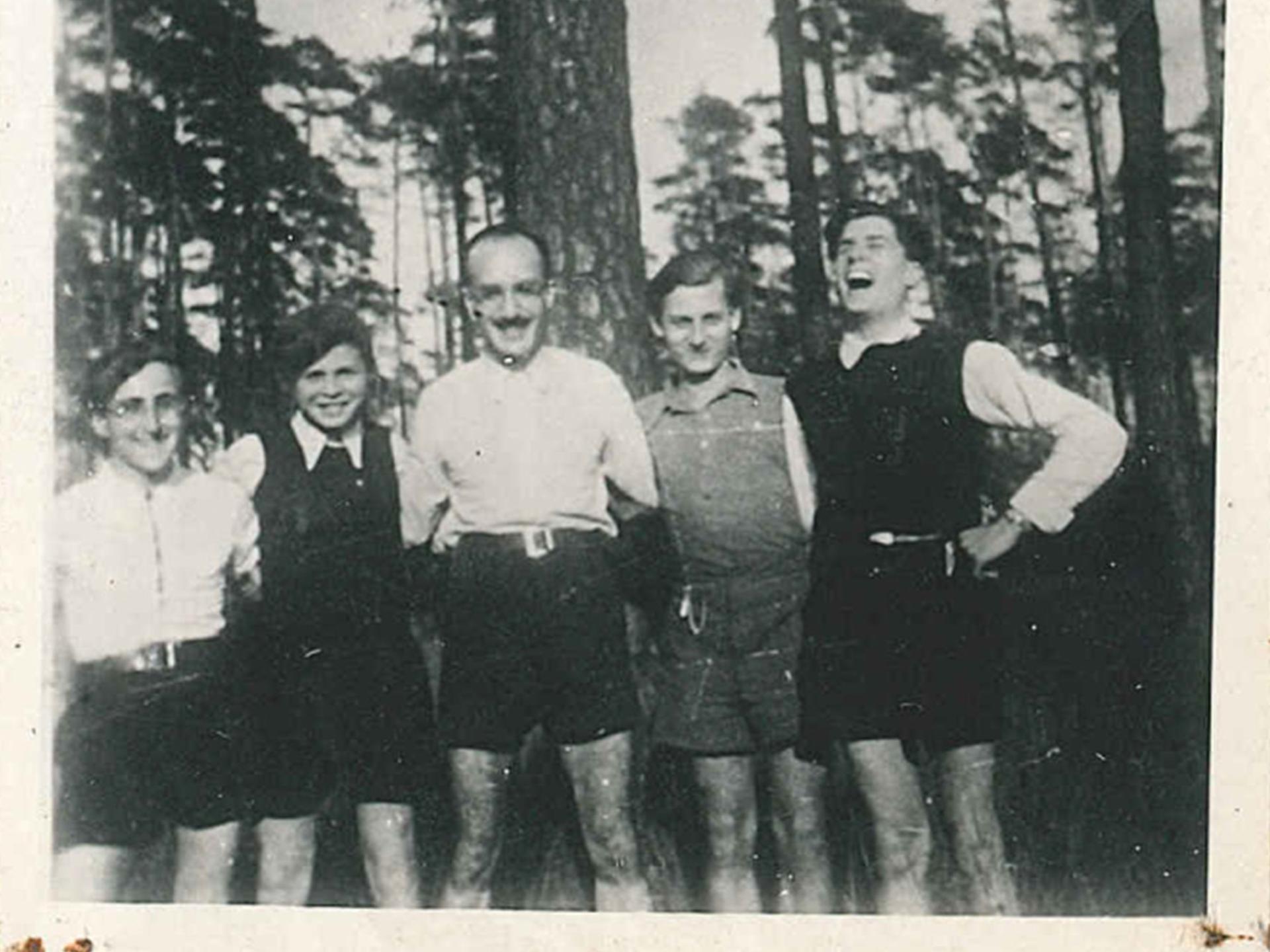 Fünf Männer stehen im Grunewald in Berlin und posieren für das Foto, sie haben sich beieinander eingehakt. Es ist in Schwarz-Weiß.
