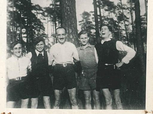 Fünf Männer stehen im Grunewald in Berlin und posieren für das Foto, sie haben sich beieinander eingehakt. Es ist in Schwarz-Weiß.
