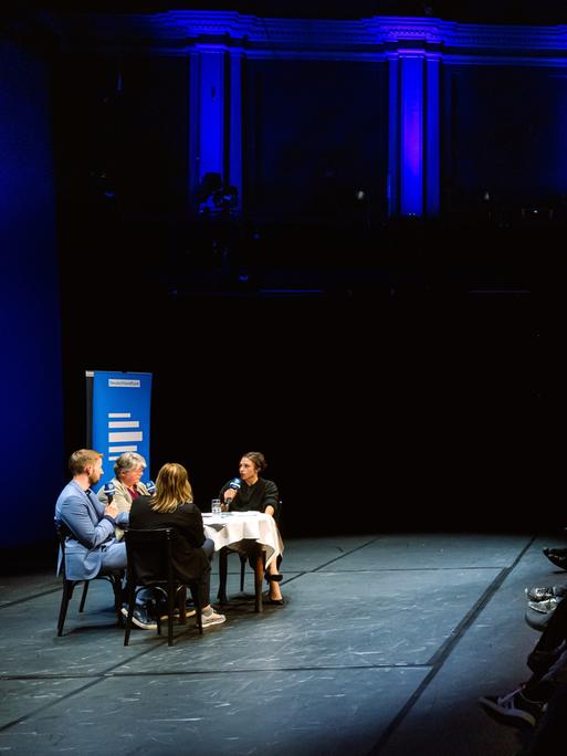 Bei der Aufzeichnung des Politikpodcasts am Neuen Theater in Halle (Saale) diskutieren Korrespondentinnen an einem Tisch, das Publikum lauscht von ansteigenden Sitzreihen. Bei der Aufzeichnung des Politikpodcasts am Neuen Theater in Halle (Saale) diskutieren Korrespondentinnen an einem Tisch, das Publikum lauscht von ansteigenden Sitzreihen.