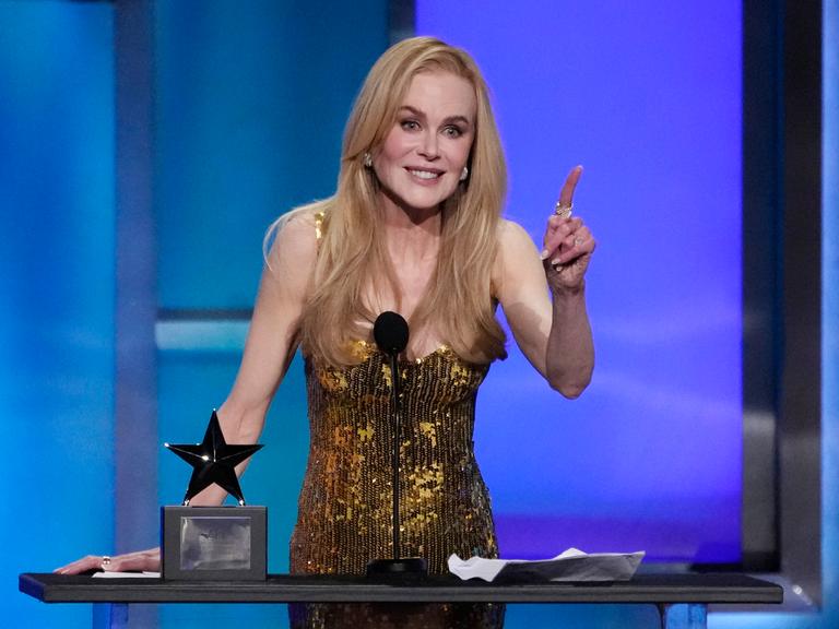 Kidman steht im goldenen Abendkleind auf der Bühne und bedankt sich für den Preis. Sie lächelt. Der Preis in Form eines schwaren Sterns steht neben ihr.