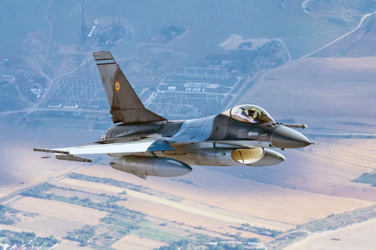 Ein F-16-Kampfjet der rumänischen Luftwaffe patrouilliert an der NATO-Ostflanke. Weit unterhalb des Jets sind Wiesen und Felder zu erkennen. 