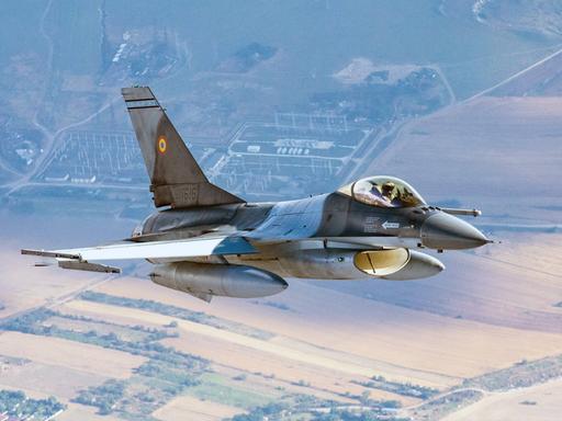 Ein F-16-Kampfjet der rumänischen Luftwaffe patrouilliert an der NATO-Ostflanke. Weit unterhalt des Jets sind Wiesen und Felder zu erkennen. 