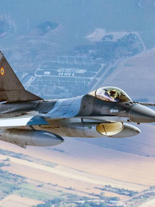 Ein F-16-Kampfjet der rumänischen Luftwaffe patrouilliert an der NATO-Ostflanke. Weit unterhalt des Jets sind Wiesen und Felder zu erkennen. 