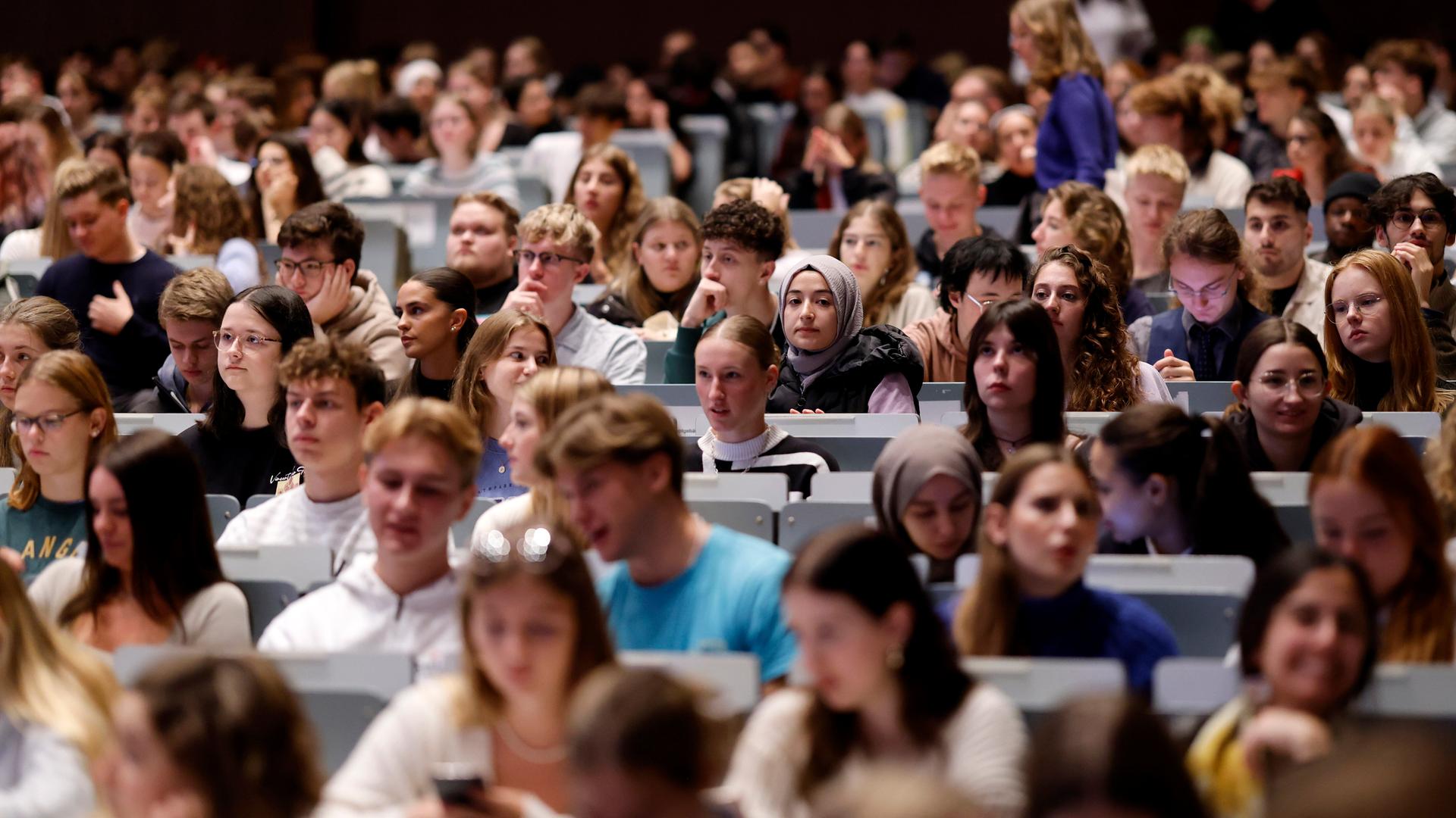 In einem großen Hörsaal sitzen viele Studierenden in den Reihen. Es sind Erstsemester bei einer Einführungsvorlesung.