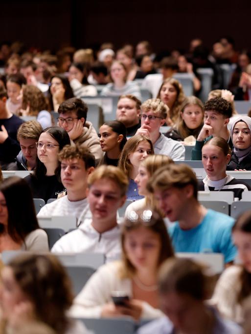 In einem großen Hörsaal sitzen viele Studierenden in den Reihen. Es sind Erstsemester bei einer Einführungsvorlesung.