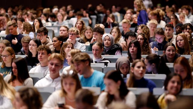 In einem großen Hörsaal sitzen viele Studierenden in den Reihen. Es sind Erstsemester bei einer Einführungsvorlesung.