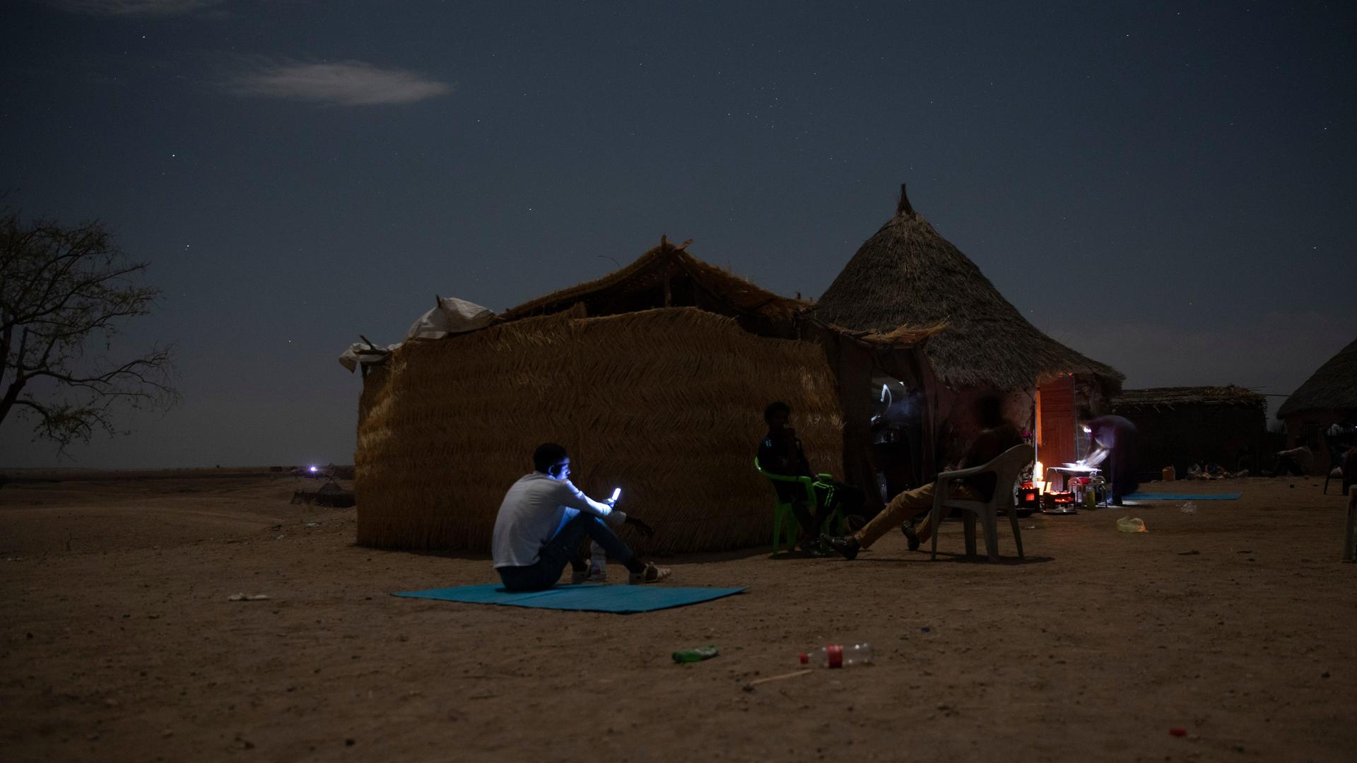 Ein Geflüchteter aus der äthiopischen Konfliktregion Tigray sitzt in der Nacht vor einer Lehmhütte und blickt auf das hell erleuchtete Display seines Mobiltelefons.